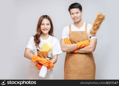 Portrait happy young couple wearing apron with rubber gloves and holding equipment with feather duster for cleaning the house together, copy space