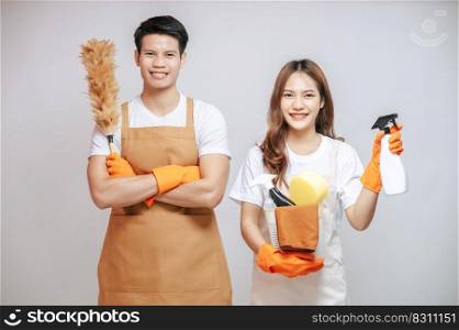 Portrait happy young couple wearing apron with rubber gloves and holding equipment with feather duster for cleaning the house together, copy space