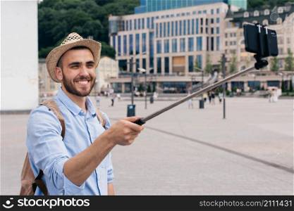 portrait happy young man carrying backpack taking selfie with smartphone