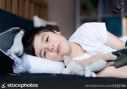 portrait healhty young boy waking up in the morning with a happy face, Kid lying in bed looking at camera with smiling face, Good sleep is important for child&rsquo;s physical and mental wellbeing concept