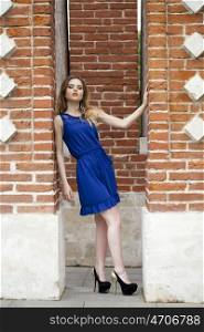 Portrait in full growth, attractive young blonde woman in blue dress against the brick wall