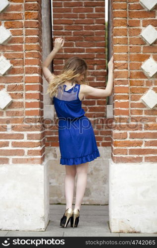 Portrait in full growth, attractive young blonde woman in blue dress against the brick wall