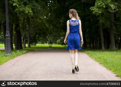 Portrait in full growth, attractive young blonde woman in blue dress walking in summer park