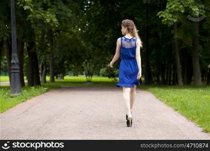 Portrait in full growth, attractive young blonde woman in blue dress walking in summer park