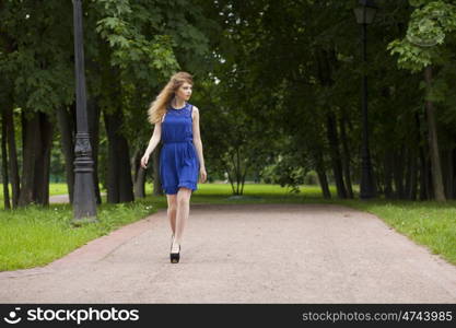 Portrait in full growth, attractive young blonde woman in blue dress walking in summer park