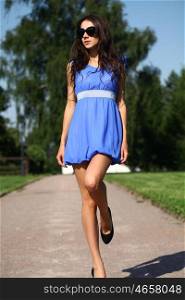 Portrait in full growth, attractive young brunette woman in blue dress walking in summer park