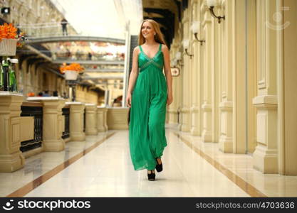 Portrait in full growth, young beautiful woman in a long green dress walking in the mall