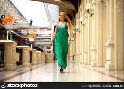Portrait in full growth, young beautiful woman in a long green dress walking in the mall
