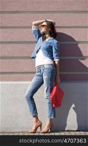 Portrait in full growth, young woman in torn blue jeans on the background wall against the wall