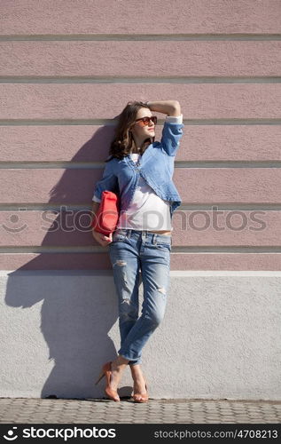 Portrait in full growth, young woman in torn blue jeans on the background wall against the wall