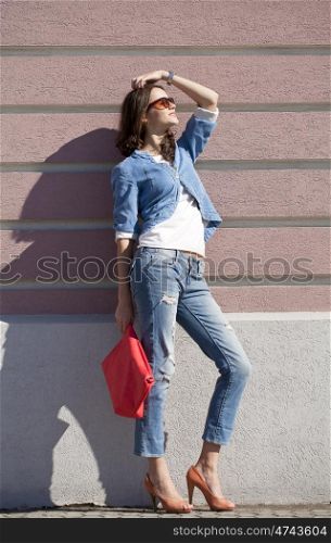 Portrait in full growth, young woman in torn blue jeans on the background wall against the wall
