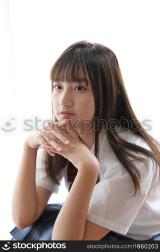 Portrait japanese school girl uniform sitting and look at camera in white tone bed room