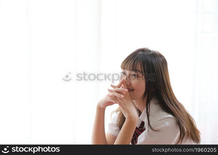 Portrait japanese school girl uniform sitting and look at camera in white tone bed room