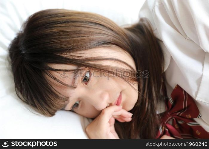 Portrait japanese school girl uniform sleep and look at camera in white tone bed room