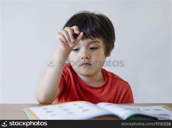 Portrait Kid boy holding black pen sitting alone and looking down with bored face ,Lonely child looking d down at table with sad face,Five years old kid bored with school homework,spoiled child