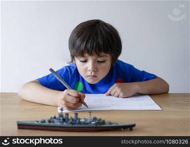 Portrait kid drawing battleship, Child boy playing with model ship toy and sketching on paper, Indoors actvitiy concept, Homeschooling