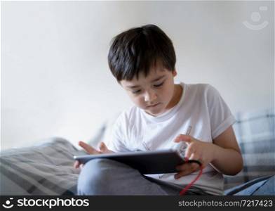 Portrait kid sitting on sofa watching cartoon on tablet,Cute boy playing game online on digital pad, Cinematic indoor portrait Child relaxing on his own in living room,Children with technology network