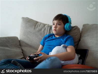Portrait kid wearing headphones and playing video game. Child holding console play game online at home, Young boy siting sofa having fun and relaxing on his own on weekend