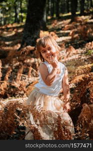 Portrait little caucasian baby girl in the forest among ferns watching away. Little caucasian baby girl squatting in the forest among ferns