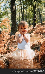 Portrait little caucasian baby girl in the forest among ferns watching away