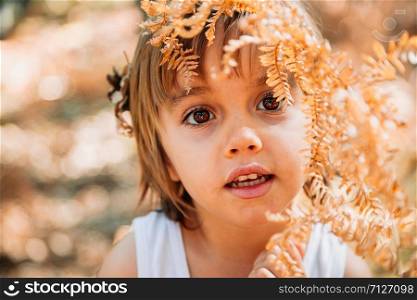 Portrait little caucasian baby girl squatting in the forest among ferns observes plants