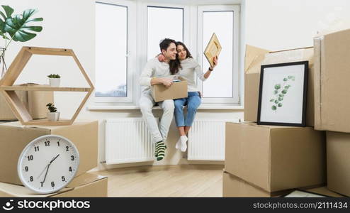 portrait loving young couple sitting window sill new apartment looking picture frame