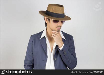 Portrait Man in Navy Blue Suit and White Shirt and Hat and Glasses Touch Chin. Man in Navy Blue suit with brown straw hat and black glasses or eyewear on grey background in smart style