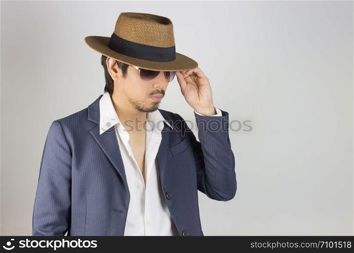 Portrait Man in Navy Blue Suit and White Shirt and Hat Touch Glasses Fashion on Side View. Man in Navy Blue suit with brown straw hat and black glasses or eyewear on grey background in smart style