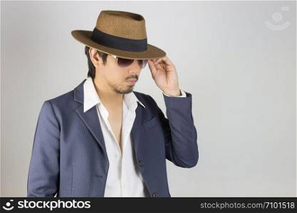Portrait Man in Navy Blue Suit and White Shirt and Hat Touch Glasses Fashion on Side View. Man in Navy Blue suit with brown straw hat and black glasses or eyewear on grey background in smart style