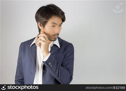 Portrait Man in Navy Blue Suit Looking Below and Touch Chin Pose. Portrait man in navy blue suit and white shirt on left frame of grey background in smart style