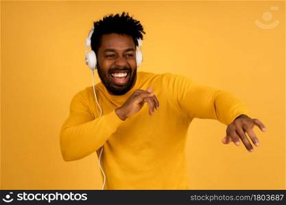 Portrait of a afro man enjoying listening to music with headphones while standing against isolated yellow background.