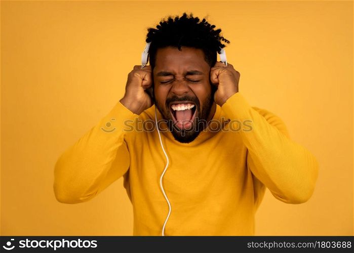 Portrait of a afro man enjoying listening to music with headphones while standing against isolated yellow background.