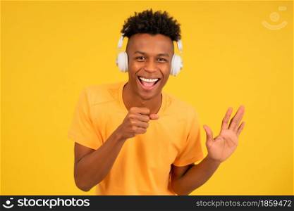 Portrait of a afro man enjoying listening to music with headphones while standing against an isolated yellow background.