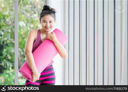 Portrait of a asian women workout practicing yoga in pink dress Hugs the Yoga mat roll pink and practice meditation wellness lifestyle and health fitness concept in a gym.