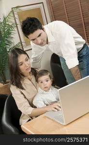 Portrait of a baby boy sitting in front of a laptop with his parents