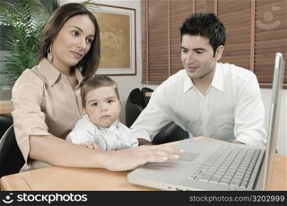Portrait of a baby boy sitting in front of a laptop with his parents