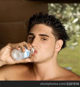 Portrait of a bare chested young man drinking water from a water bottle