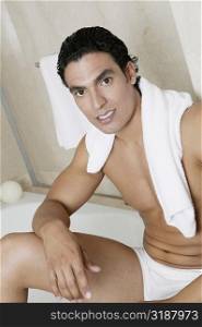 Portrait of a bare chested young man sitting at the edge of a bathtub