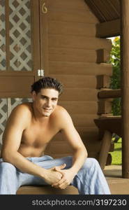 Portrait of a bare chested young man sitting on the porch and smiling