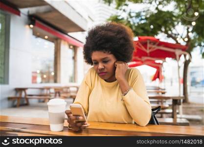 Portrait of a beautiful afro american latin woman using her mobile phone while sitting on coffee shop. Communication concept.