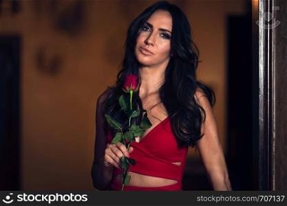 Portrait of a beautiful and elegant woman holding a rose in an evening red dress