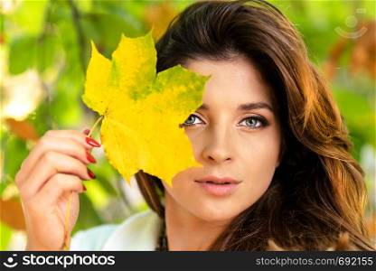 Portrait of a beautiful and lovely young woman holding fallen leaf and posing in the park on a sunny day.