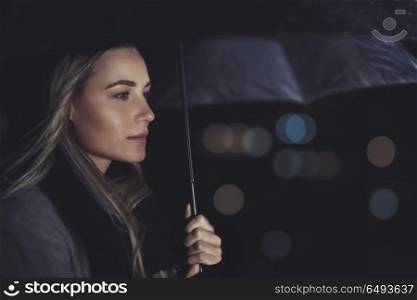 Portrait of a beautiful authentic woman standing under umbrella in rainy night, conceptual photo of loneliness and sadness. Beautiful woman under the rain