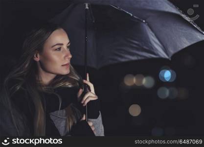 Portrait of a beautiful authentic woman standing with an umbrella on rainy night, conceptual photo of loneliness and sadness. Beautiful woman under the rain