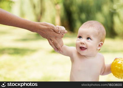 Portrait of a beautiful baby holding the mother’s hand against green nature background outdoors