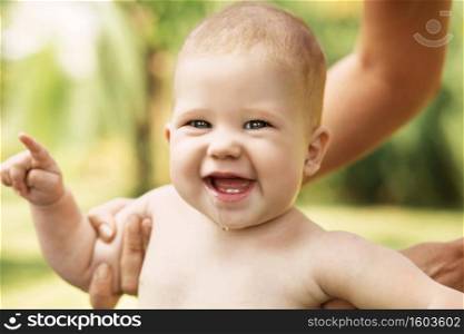 Portrait of a beautiful baby holding the mother’s hand against green nature background outdoors