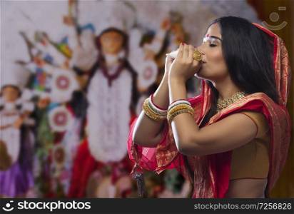 Portrait of a beautiful Bengali woman blowing conch shell at Durga puja