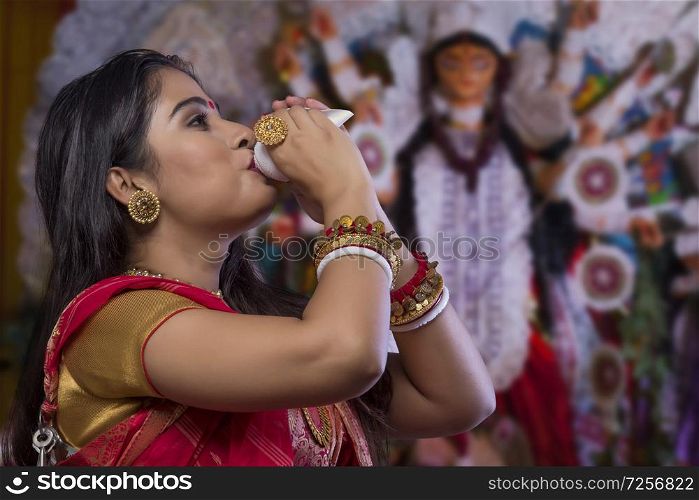 Portrait of a beautiful Bengali woman blowingconch shell at Durga puja