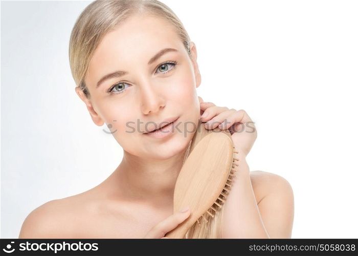 Portrait of a beautiful blond girl combing her hair isolated on white grey background, fashion model with natural makeup and healthy strong hair