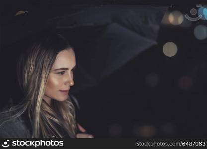 Portrait of a beautiful blond girl waiting for someone at dark rainy night, fashion women&rsquo;s portrait with umbrella over blurry night city lights background. Beautiful woman at rainy night